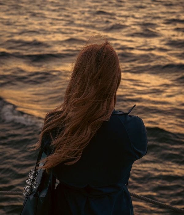 A woman meditating outdoors with her back to the camera, facing a scenic view.